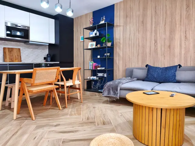 Salón-comedor de Lo Peix con pared azul, cocina abierta y mesa de madera